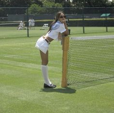 a woman leaning on a tennis court fence