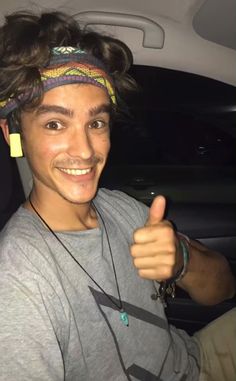 a young man in a car giving the thumbs up sign with his headband on