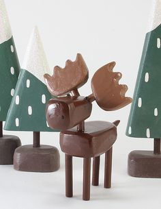 three small wooden reindeer figurines in front of some trees with white dots on them