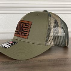 American Flag Eagle Patriotic Leather Patch Hat Green/Camo. Specifications: 🧢 Richardson original 112 trucker; adjustable for the perfect fit 🎩 60/40 cotton/polyester blend for comfort 📏 One size fits most 🏷️ Expertly laser engraved leatherette patch design 📦 Ships in 2 to 3 business days from our Orlando Studio Care Instructions: 🚫 Do not wash; spot clean only Please Note: 🌈 Colors may vary from photos based on your viewing screen. This funny hat is a unique and entertaining gift for fathers, embracing their dual role with humor. Brown Military Hat, One Size Fits Most, Brown Military Style Trucker Hat, Brown Military Trucker Hat, Adjustable Khaki Snapback Hat With Flat Bill, Adjustable Camouflage Flat Bill Hat, Adjustable Khaki Flat Bill Hat, Adjustable Flat Bill Hat In Khaki, Military Style Adjustable Flat Brim Baseball Cap, Military Style Adjustable Baseball Cap With Flat Brim