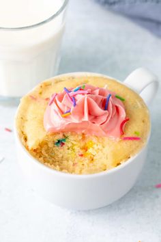 a cupcake with pink frosting and sprinkles next to a glass of milk