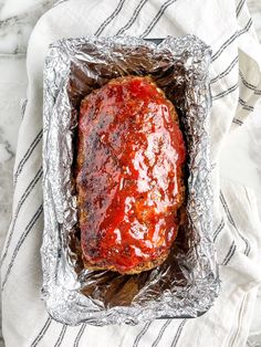 a meatloaf covered in ketchup sitting on top of tin foil next to a white towel