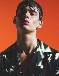 a young man with his eyes closed wearing a shirt and necklace, against an orange background