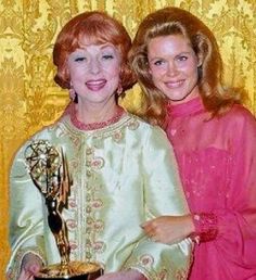 two women standing next to each other in front of a curtain holding an award trophy