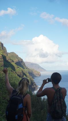 two people looking out at the ocean while taking pictures