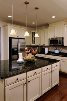 a large kitchen with white cabinets and black counter tops, along with an island in the middle