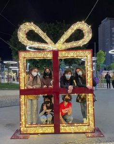 people wearing face masks and standing in front of a christmas present box with lights on it