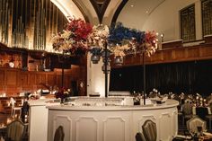 a bar with flowers and candles on it in a room filled with tables, chairs and chandeliers