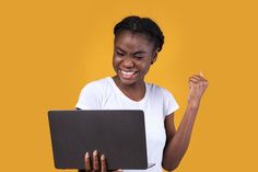 a woman holding a laptop computer in her right hand and smiling at the camera with both hands