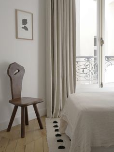 a bed room with a neatly made bed and a wooden chair next to the window