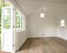 an empty room with wood floors and white walls, windows on the far wall are open