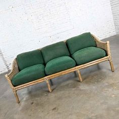 a green couch sitting on top of a cement floor next to a white brick wall