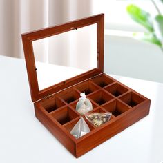 an open wooden box with tea bags in it on a white table next to a potted plant