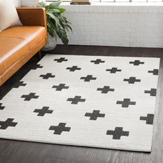 a white rug with black crosses on it in front of a brown leather couch and window