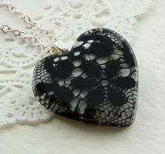 a black and white heart shaped pendant on a silver chain with lace doily around it