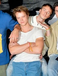 three young men sitting next to each other in front of a wall with their arms crossed