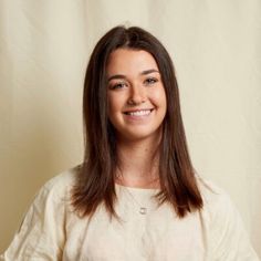 a woman with long brown hair smiles at the camera while standing in front of a white backdrop