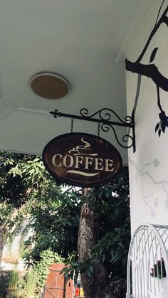 a coffee shop sign hanging from the side of a white building next to a tree