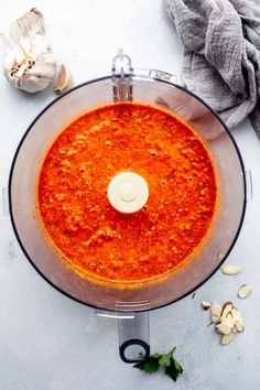 an overhead view of a food processor with red sauce in it and garlic on the side