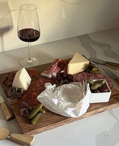 a wooden cutting board topped with cheese and meats next to a glass of wine