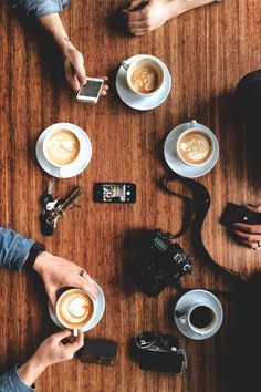 people are sitting at a table with cups of coffee and cell phones in front of them