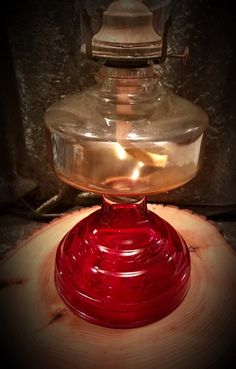 a red glass jar sitting on top of a wooden table next to a light bulb