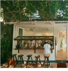 a man standing in front of a small bar with stools and plants on the roof