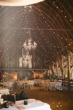 the inside of a barn with tables and chandeliers