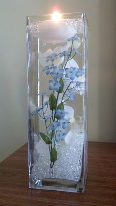 a glass vase with flowers in it on a table next to a candle and some water