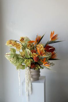 an arrangement of flowers in a vase sitting on a white pedestal against a gray wall