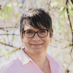 a woman wearing glasses standing in front of a tree with no leaves on her head