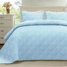 a bed with blue comforter and pillows in a room next to a dresser,