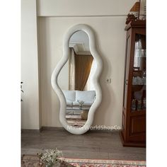 a large white mirror sitting on top of a wooden floor next to a wall mounted cabinet