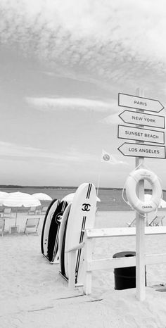 surfboards and life preservers on the beach with signs pointing to different locations in black and white