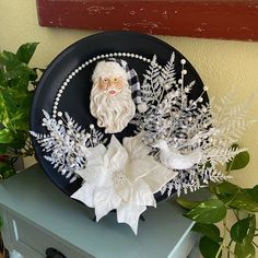 a black plate with white flowers and a santa clause decoration on the side next to a potted plant