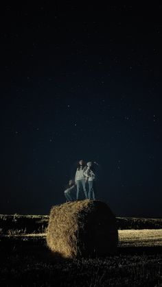 two people standing on top of a bale of hay at night with stars in the sky