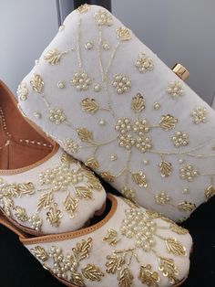 a pair of white shoes with gold beading on them and a handbag in the background