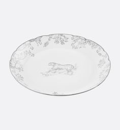 a white plate with an animal design on the side and flowers in the middle, against a gray background