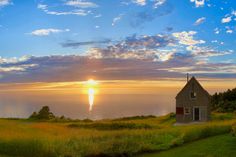 the sun is setting over an old house by the ocean