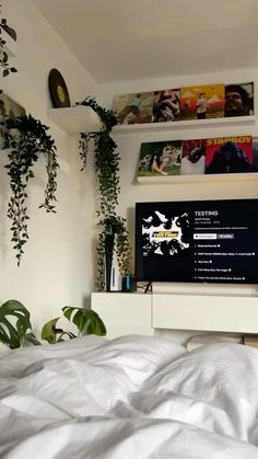 a flat screen tv sitting on top of a white dresser next to a plant filled wall