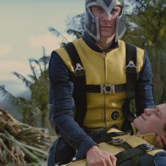 a man in a yellow and black outfit sitting next to another man wearing a helmet