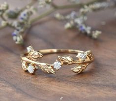 a close up of a gold ring with leaves and diamonds on it, sitting on a wooden surface