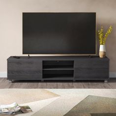 a large flat screen tv sitting on top of a wooden entertainment center next to a vase with flowers