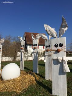 three wooden bunny statues in the grass next to an egg and hay bale filled with hay