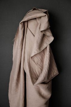 an unbuttoned coat hanging up against a black wall with the hood pulled back