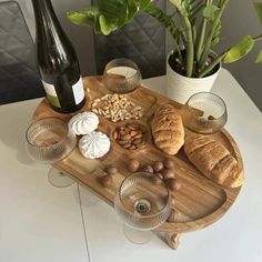 a wooden tray with bread, nuts and wine on it next to a potted plant