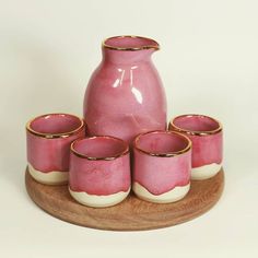 a pink and white vase sitting on top of a wooden tray with gold rimmed glasses