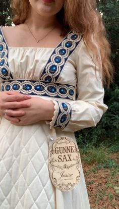 A rare Gunne Sax dress with its original tags!Absolutely amazing 1970s Gunne Sax dress. Renaissance style in cream cotton with empire waist, square neckline, quilted skirt, and blue floral embroidered trim. The original tags are still attached and it doesn't seem to have ever been worn. Zips up back center and has a sash that ties in the back as well.Condition: The inside of the skirt has a small stain that can be seen a bit on the outside. It may come out with washing -- I haven't tried as I didn't want to remove the tag. The stain is small and light, in my opinion not noticeable. See last photo.Measurements- This is a vintage size 9, but it doesn't fit like a modern 9 so please review the measurements carefully.- Bust: 33 inches (There's a little wiggle room here because the neck has ela Vintage Gunne Sax Dress, Flower Maxi Dress, Quilted Skirt, Sax Dress, Gunne Sax Dress, Embroidered Trim, Dress Cream, Gunne Sax, Blue Trim