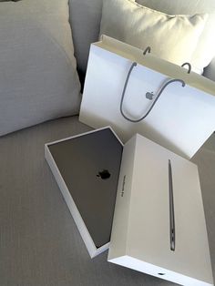 an apple laptop sitting in a box on top of a couch next to a pillow