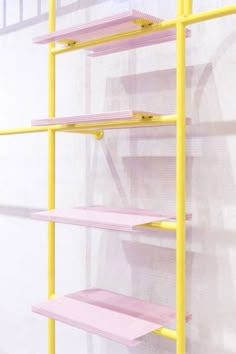 a yellow metal shelf with pink shelves on the side and white wall behind it,